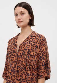 Brun leopardmønster skjorte med en avslappet passform, korte ermer, krage og en brystlomme. Materialet ser glatt og litt skinnende ut.