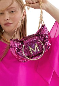 Bolso de mano de lentejuelas rosas con cadena dorada y acento de logotipo circular. Presenta una forma suave y una textura brillante.
