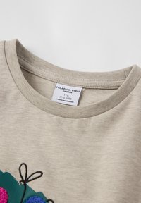Beige katoenen t-shirt met ronde hals en textuurstof. Voorzien van kleurrijke geborduurde bloemen en een label met maat en herkomst.