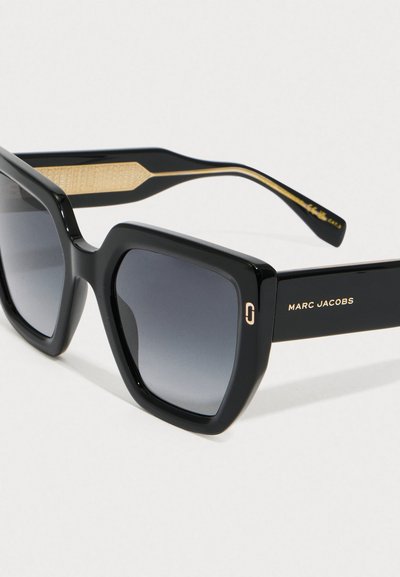 Gafas de sol cuadradas de gran tamaño en color negro con lentes oscuros en degradado y detalle dorado, mostrando el nombre de la marca "Marc Jacobs" en la patilla.