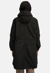 Czarna parka z kapturem, z regulowanym pasem, długimi rękawami i gładką teksturą. Posiada prosty krój, minimalistyczny design i brak widocznych logotypów.