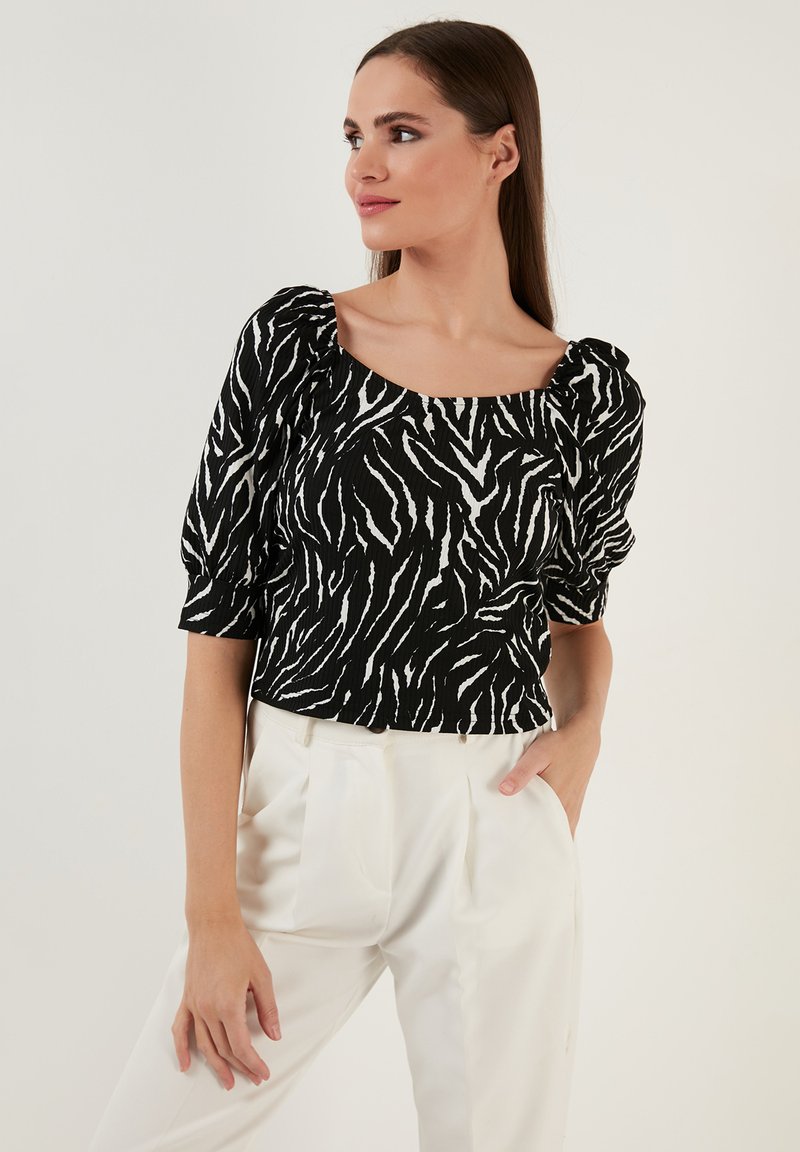 Bluse med puffede ærmer i sort og hvid striber og firkantet udskæring. Stoffet har en struktureret overflade, som komplementerer det markante mønsterdesign.