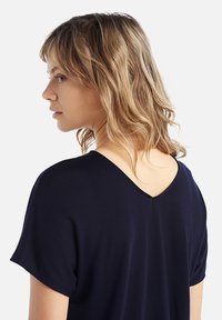 Top navy a V con maniche corte, caratterizzato da una schiena scollata e una texture morbida e liscia. Design semplice senza fantasie o accessori.