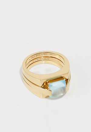 Gold-tone ring featuring a smooth, light blue stone with a rectangular shape. The design includes stacked bands with a polished finish.