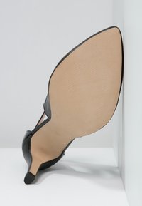 Chaussure noire à talon haut avec un bout pointu et un talon fin. La semelle est lisse beige avec un léger détail texturé.