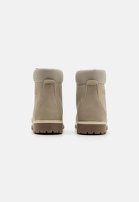 Beige lær ankle boots med en blød grå krave, hvid syning og en tekstureret gummisål, der har et simpelt logodesign på siden.