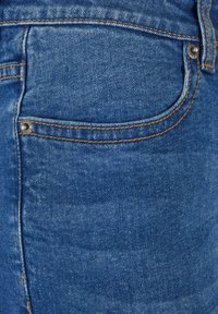 Vaqueros de mezclilla azul con un diseño clásico, que cuentan con un bolsillo trasero y costuras en un color amarillo-naranja contrastante. Detalle del botón metálico visible.