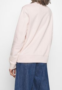 Felpa rosa chiaro con una vestibilità comoda, scollatura rotonda e polsini a coste. Il tessuto appare morbido con una consistenza liscia. Indossata con jeans a gamba larga.