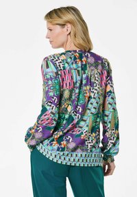 Blusa colorata con un mix di motivi floreali e geometrici, con maniche lunghe e retro arricciato, realizzata in un materiale morbido e fluido.