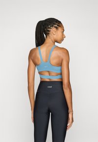 Reggiseno sportivo blu a coste con spalline larghe e design con schiena scoperta, abbinato a leggings neri a vita alta con dettaglio del logo.