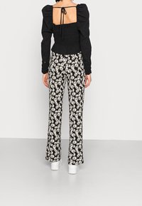 Haut noir à manches bouffantes avec dos carré et détail à nouer, associé à un pantalon taille haute évasé avec un imprimé marguerite blanche sur fond noir.