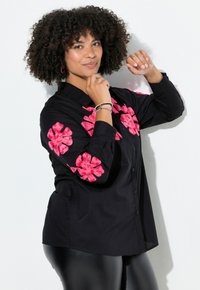 Schwarzes Hemd mit langen Ärmeln, das rosa Blumenstickereien an den Schultern aufweist. Der Stoff wirkt glatt und hat ein Mit-Knöpfen-Design.