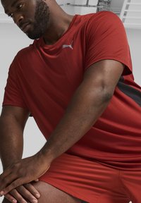 Camiseta atlética roja de manga corta, con tejido texturizado, que presenta un pequeño logo azul. Combinada con pantalones cortos rojos a juego.