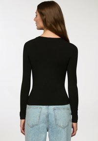 Czarny sweter z długim rękawem o dopasowanym kroju i ściągaczami na mankietach, zestawiony z jasnoniebieskimi spodniami z wysokim stanem, które mają tylne kieszenie.