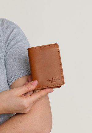 Brun lædermappe med stikninger i kanterne, bifold design og præget logo. Glat tekstur med en kompakt størrelse, holdt mellem fingrene.