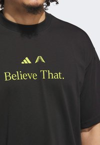 Sort bomuld T-shirt med rund hals, korte ærmer og et gult grafisk tryk med teksten "Believe That." samt logo detaljer.