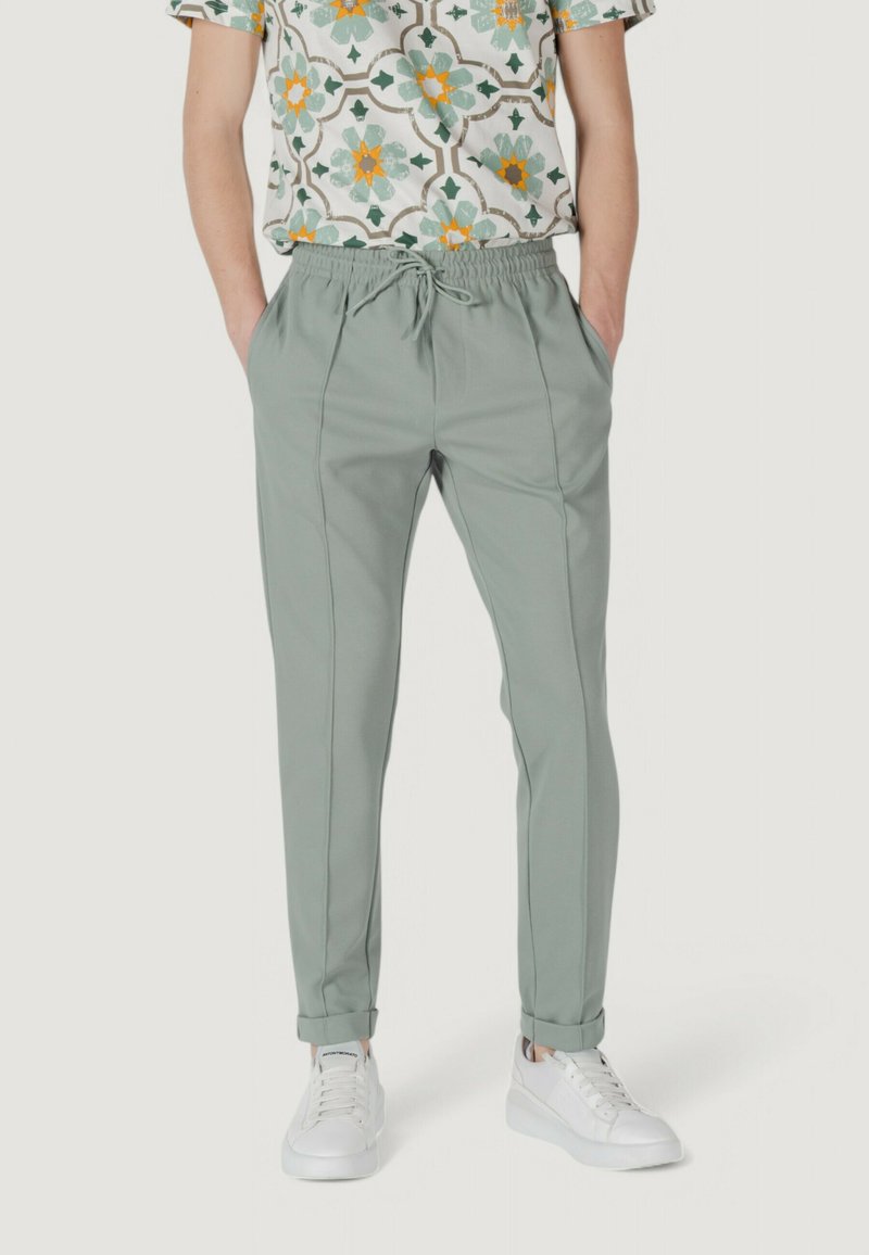 Pantaloni leggeri verdi chiaro da uomo con vestibilità affusolata, dotati di tasche laterali e orli arrotolati, abbinati a una camicia con motivo.