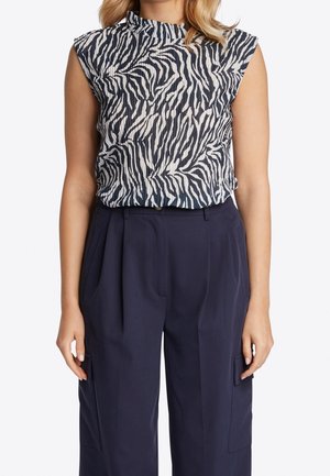 Short-sleeve blouse in a navy and white zebra print, featuring a ruffled neckline. Paired with tailored, high-waisted navy trousers.