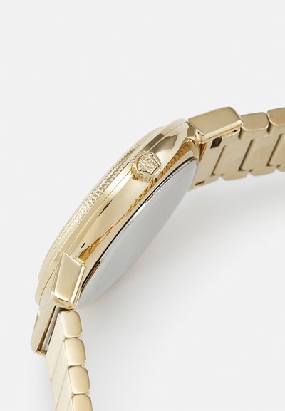 Küljepoolt vaade kuldse metallkellaga, millel on tekstureeritud kroon, millel on lõvipea embleem.