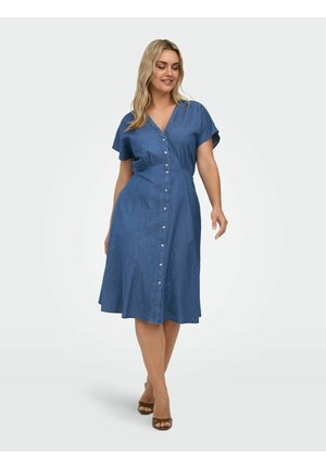 Naine kannab sinist nööpidega midi-pikkust kleiti lühikeste varrukatega, kõnnib kergelt naeratades ja pruunide avatud varbaga kontsadega.