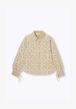 Blouse beige à manches longues avec découpes en dentelle florale, fermeture boutonnée devant, col pointu et liens aux poignets.