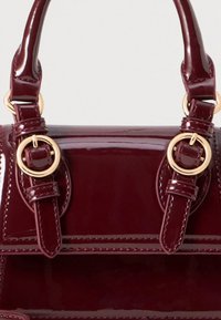 Bordeauxfarbene Handtasche aus Lackleder mit goldfarbenen Beschlägen, zwei oberen Griffen, Knopfakzenten und detaillierten Nähten entlang der Nähte.