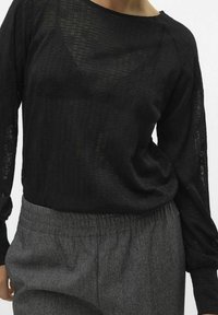 Kvinna som bär en svart genomskinlig långärmad topp med blommönster och grå byxor med elastisk midja.