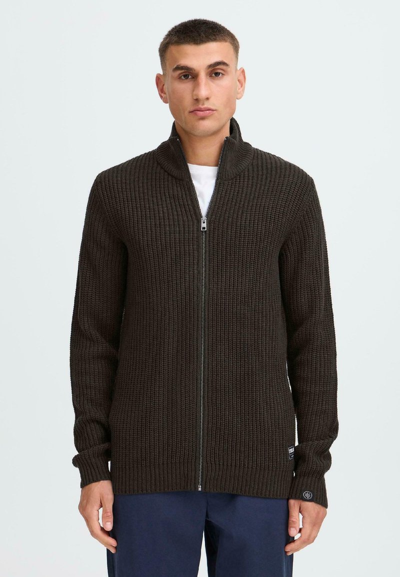 Dunkelbrauner gerippter Strickzipper mit hohem Kragen und langen Ärmeln, mit einem kleinen Logo-Detail am Bündchen. Einfarbig.