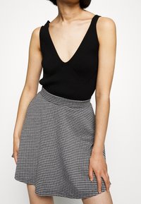 Musta ribbineuloksinen toppi, jossa syvä V-pääntie, yhdistettynä mustavalkoiseen ruudulliseen kellohameeseen, jossa on istutettu vyötärö ja pehmeä tekstuuri.