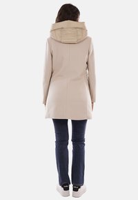 Cappotto beige con cappuccio imbottito, maniche lunghe e taglio dritto. Abbinato a jeans blu scuro e sneakers bianche con dettagli neri.