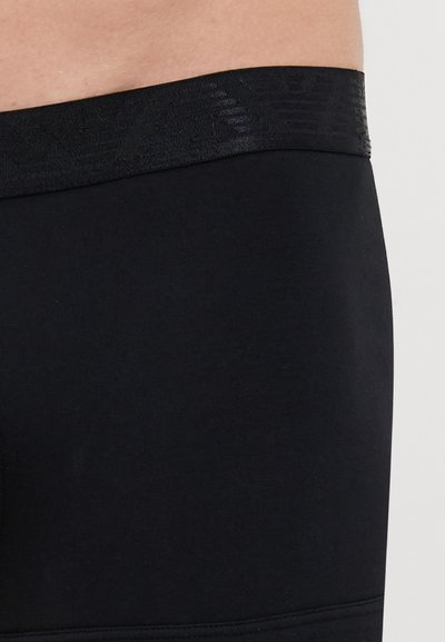 Fekete leggings sima felülettel és széles, mintás derékpánttal. Szoros szabású dizájn jellemzi. Nincsenek további minták vagy díszítések.