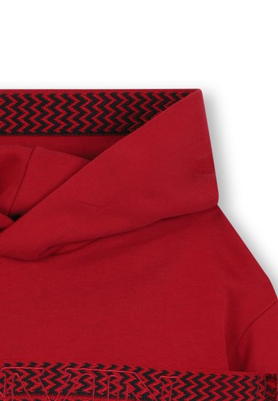 Felpa rossa con cappuccio caratterizzata da un design a zigzag nero sul cappuccio e sull'orlo, realizzata in tessuto morbido con una consistenza liscia.