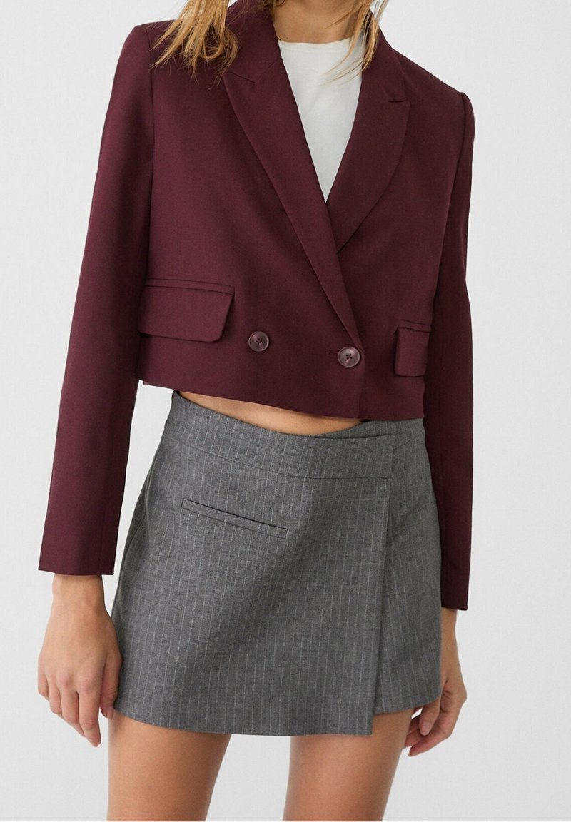 Bordeaux cropped blazer met twee knopen, voorzien van zijzakken, gecombineerd met een grijs gestreepte minirok met een asymmetrische zoom.