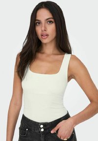 Bodysuit blanco sin mangas con escote cuadrado y diseño ajustado, combinado con jeans negros de tiro alto que cuentan con detalles de botones.