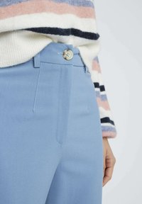 Pantalons taillés bleu clair en tissu lisse avec un bouton et une fermeture éclair visibles, dotés de poches avant plates et de détails de couture soignés.