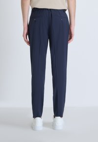 Marineblauwe op maat gemaakte broek met een elastische tailleband, voorzien van twee achterzakken met knopen en een recht gesneden ontwerp. Gladde stoftextuur.