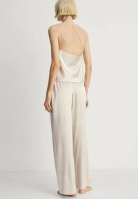 Satin komplet koji se sastoji od bezrukavog topa s tankim naramenicama i širokih, lepršavih hlača u svijetloj bež boji. Glatka tekstura.