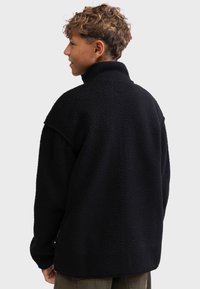 Black fleece pullover with a high collar, textured surface, and relaxed fit. Features shoulder seams and a tag at the hem.