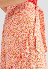 Bloemenrok in het roze, met oranje en gele bloemenpatronen, zachte stof en gerimpelde randen met een strikdetail in de taille.