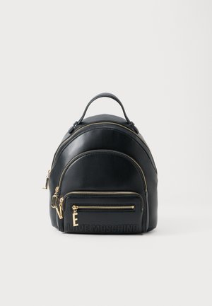 Mochila preta de couro com um design arredondado, fechos dourados e um bolso frontal com detalhe em relevo do logo. Inclui uma alça superior.