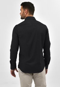 Zwart overhemd met lange mouwen, gemaakt van gestructureerde stof, met een button-down kraag en manchetten, een gebogen zoom en een getailleerde pasvorm.
