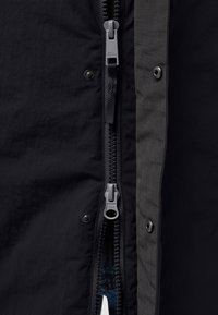 Giacca nera con doppio zip, accento grigio, chiusura a scatto e tessuto texturizzato con motivo a griglia lungo il lato destro.