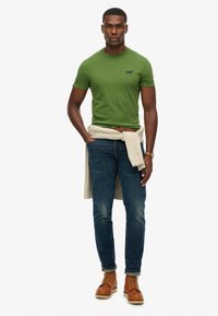 Grøn bomulds t-shirt med rund hals, parret med blå jeans og brune støvler. En let sweater er bundet om taljen.