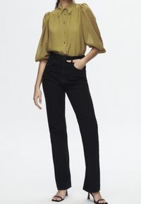 Blouse à manches bouffantes à carreaux vert olive avec col pointu, assortie à un jean noir taille haute et des sandales à talons ouverts noires.