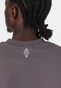 Šedé bavlněné tričko s kulatým výstřihem, na zadní straně s bílým výšivkovým logem ve tvaru diamantu. Krátké rukávy, hladká textura.