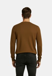 Maglione marrone testurizzato con scollo rotondo e maniche lunghe, abbinato a jeans neri, visto da dietro su uno sfondo chiaro.