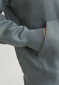 Grey sweatshirt with a smooth texture, featuring a spacious front pocket and ribbed cuffs. Close-up view highlights sleeve detail.