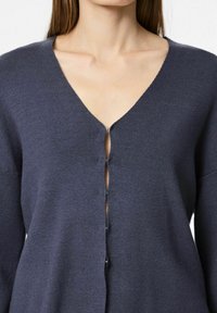 Suéter azul marino oscuro con diseño de cuello en V, con cierre de botones en la parte delantera y textura de punto. Se aprecian las mangas largas y un ajuste relajado.