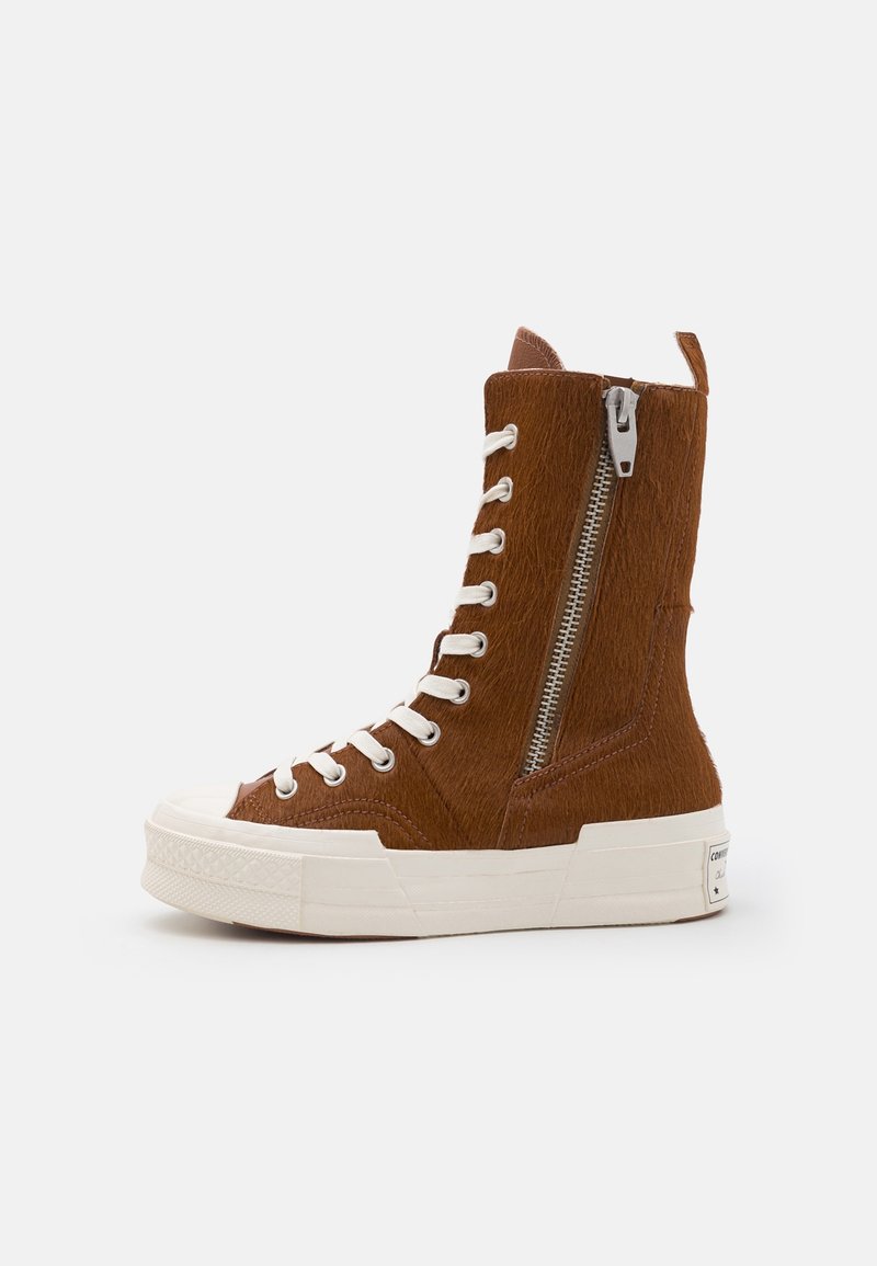 Bottine sneaker montante marron avec lacets blancs, fermeture éclair latérale, semelle en caoutchouc et matériau texturé, montrée de profil sur fond blanc.