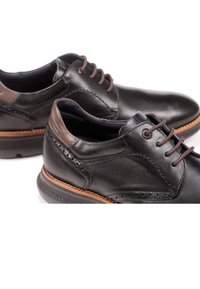 Zapatos de cuero negro con detalles en marrón, con una textura suave y perforaciones decorativas. Diseño con cordones y suela ligera.